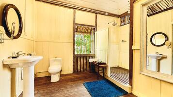 A bathroom with wooden floors, a white sink, a toilet, and a shower area.