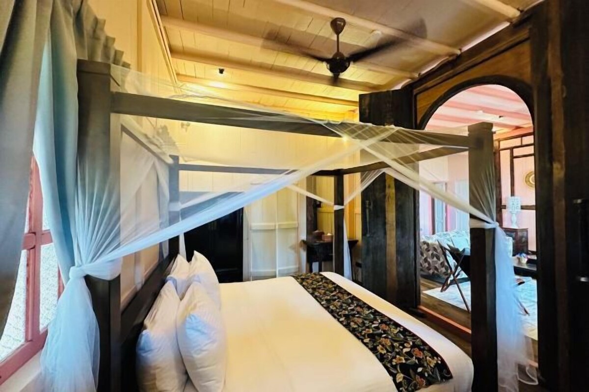 Une chambre avec un lit sous une moustiquaire, un plafond en bois et une vue sur le paysage, visible à travers une porte en arc de cercle.