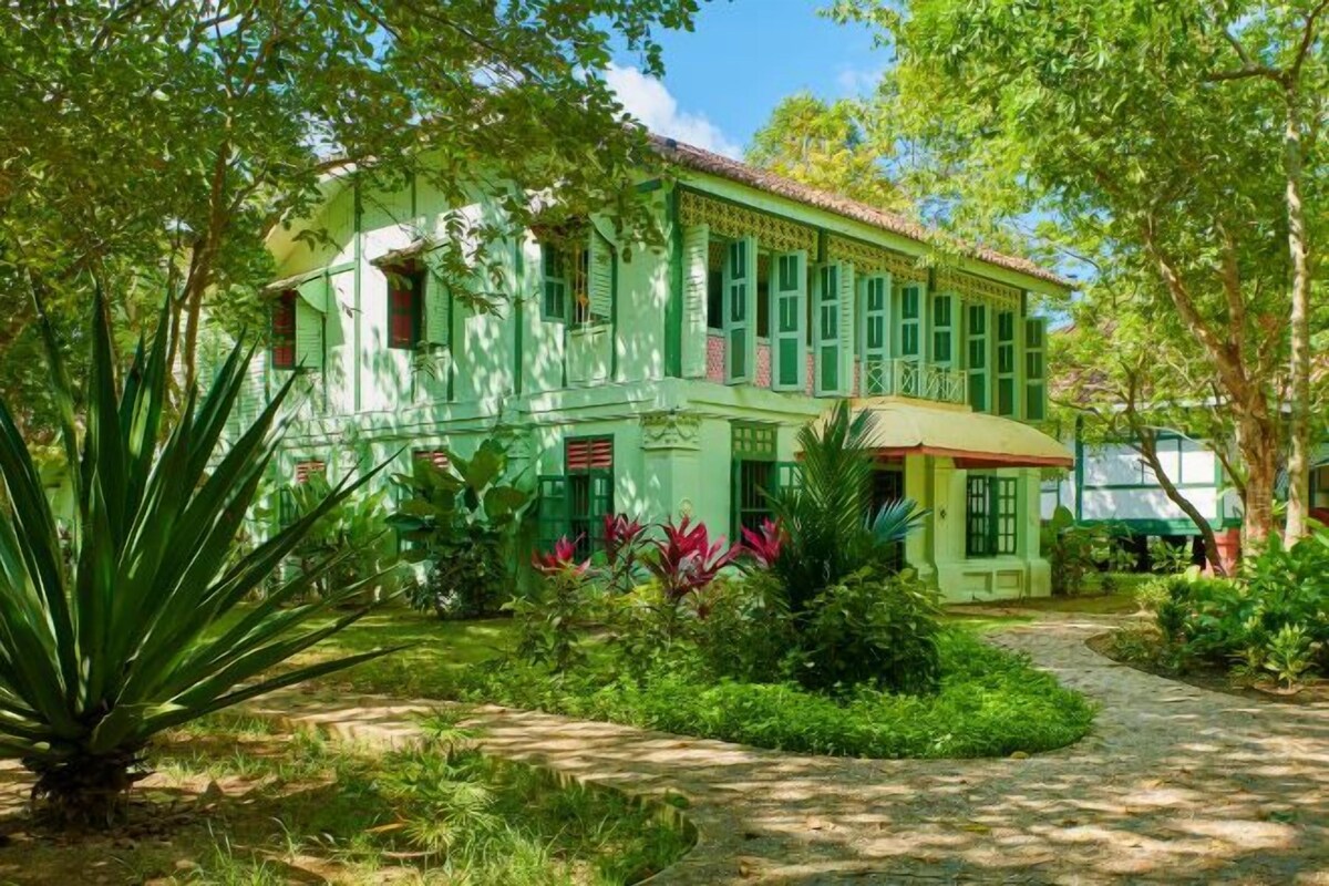 A traditional green colonial-style building with a garden pathway leading to the entrance.