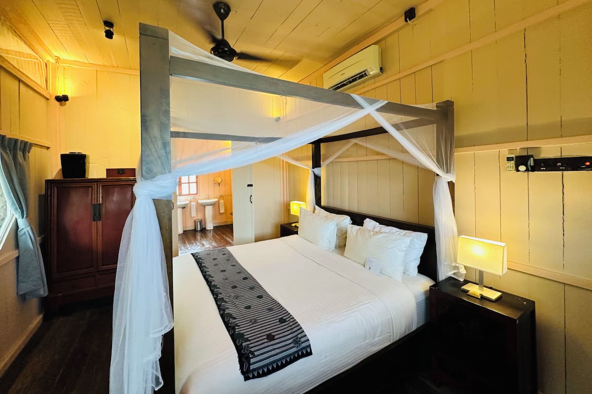 Un dormitorio con una cama con dosel, un ventilador de techo, un equipo de aire acondicionado y una mesita de noche con lámpara.
