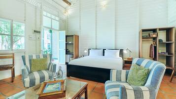 A spacious bedroom with a large bed, two striped armchairs, a glass coffee table, and a wooden side table.