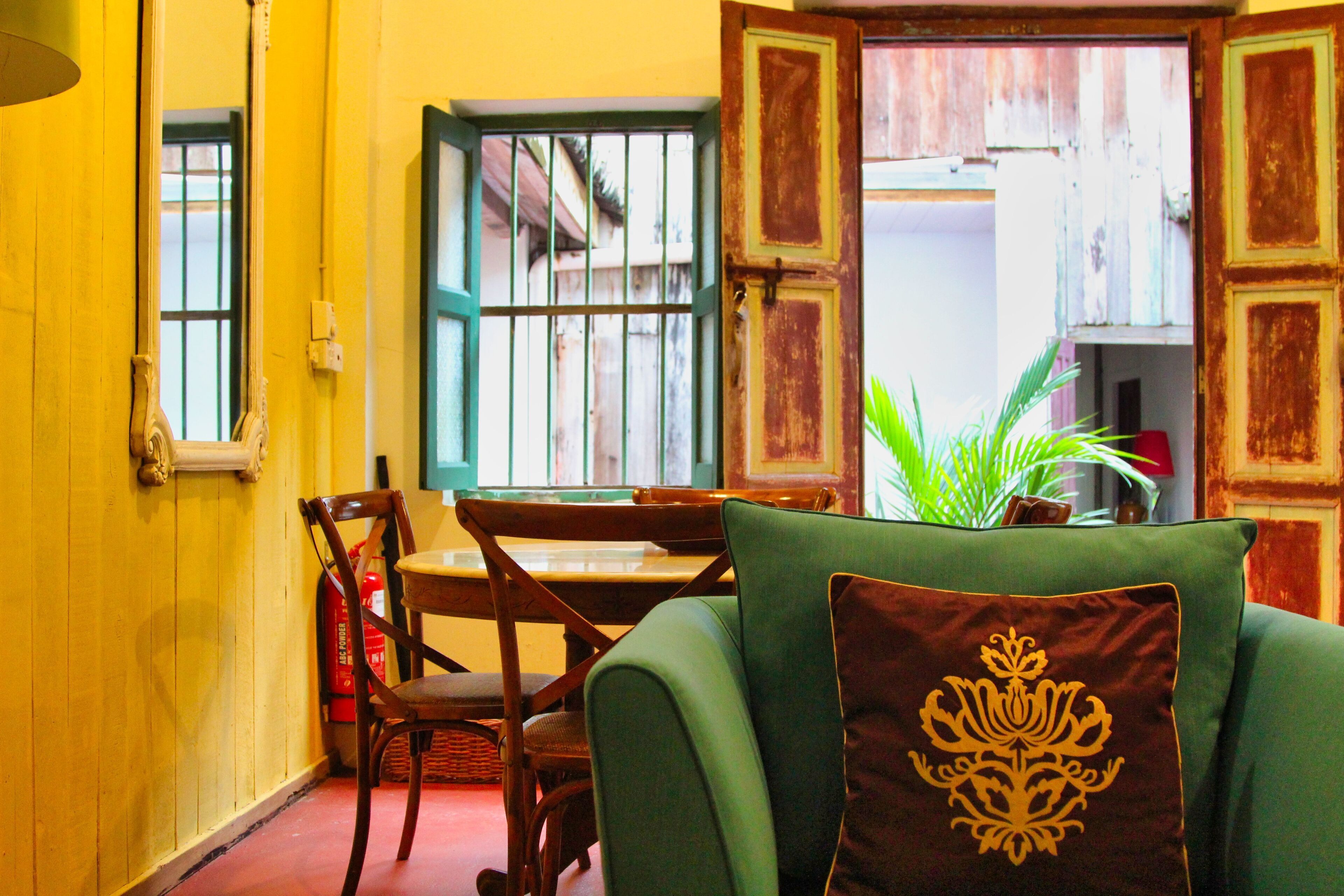 A room with a green sofa, a wooden dining table, chairs, and a window with a view of the outside.