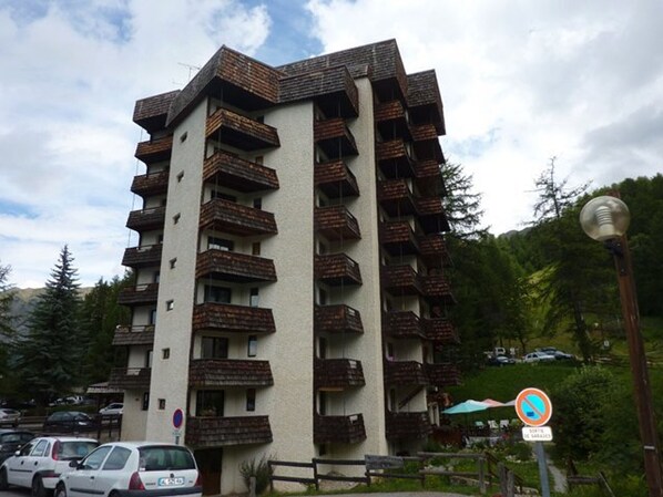 A multi-story building with balconies, a parking area with cars, and a no parking sign.