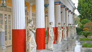 A corridor with statues and columns, a checkered floor, and a building facade with yellow and white colors. - Villa Evanna (Corfu)