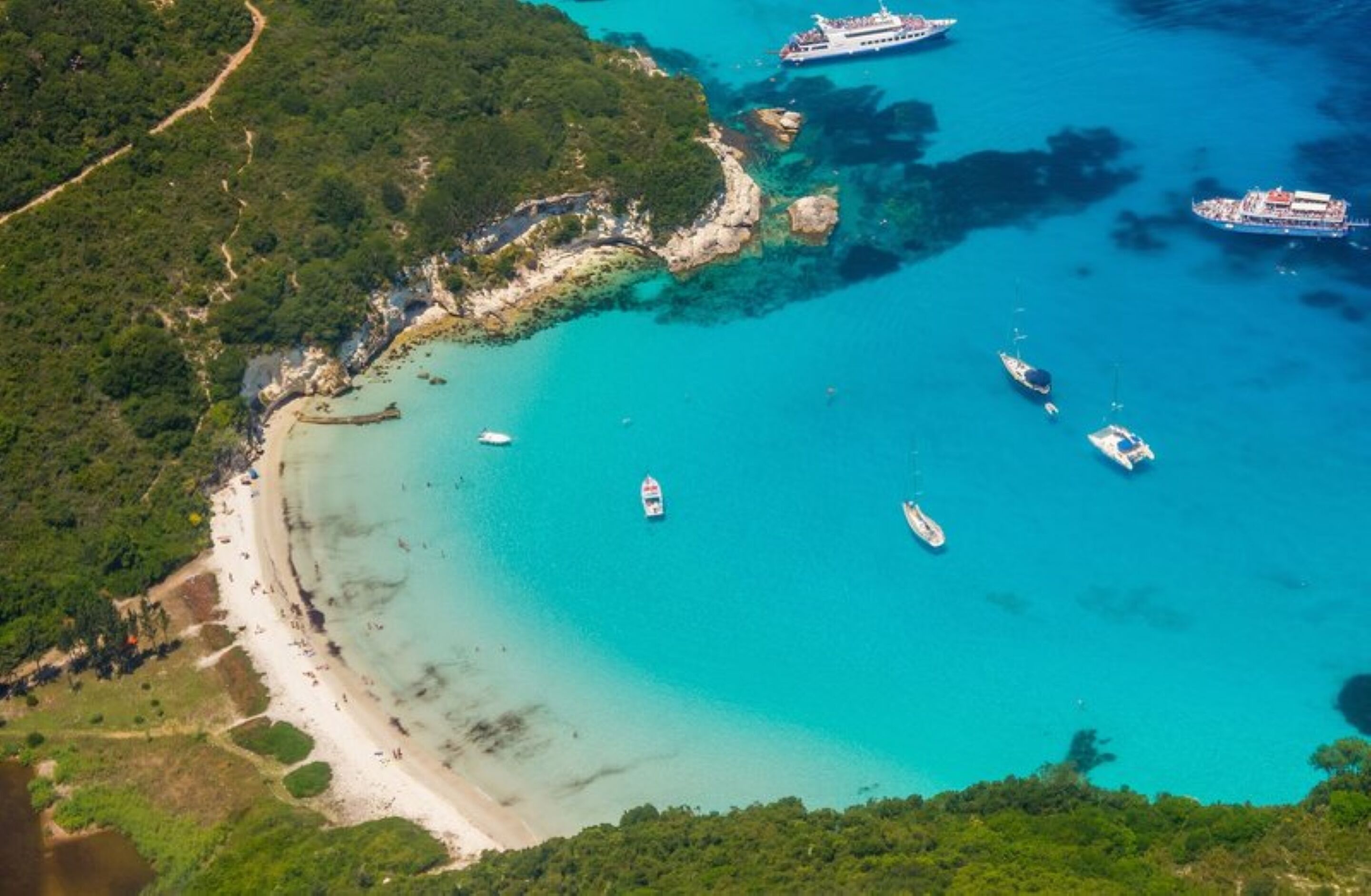 Eine Vogelperspektive einer Küstenlandschaft mit Strand, Booten und einem Kreuzfahrtschiff, das in der Nähe der Küste liegt.