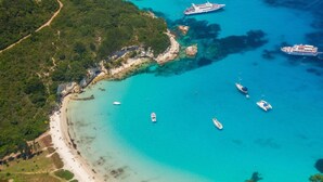 An aerial view of a coastal area with a beach, boats, and a cruise ship docked near the shore. - Villa Evanna (Corfu)
