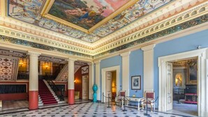 A grand hall with a high ceiling, ornate ceiling decorations, a marble floor, and classical columns. - Villa Evanna (Corfu)