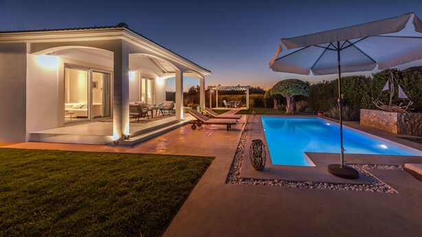 A modern outdoor pool area with a covered seating area, lounge chairs, and a well-lit patio. - Villa Evanna (Corfu)