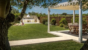 A covered patio area with a table and chairs, a stone wall, and a well-maintained lawn. - Villa Evanna (Corfu)
