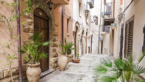 A narrow alleyway with stone walls, potted plants, and a wooden door. - Terrazza Gabbiano Sopra (Cefalù)