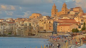 Un pueblo costero con edificios históricos, una iglesia destacada y una zona de playa con sombrillas y gente.