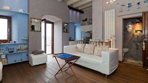 Ein Wohnzimmer mit einem weißen Sofa, einem Couchtisch und Holzboden. Im Hintergrund ist eine Küchenzeile mit Herd und Schränken zu sehen.