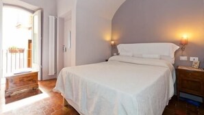 Ein Schlafzimmer mit einem großen Bett, einer hölzernen Bank, einer Tür, die auf einen Balkon führt, und einer Wandleuchte.