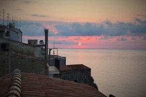 A coastal view with buildings and a sunset over the sea.