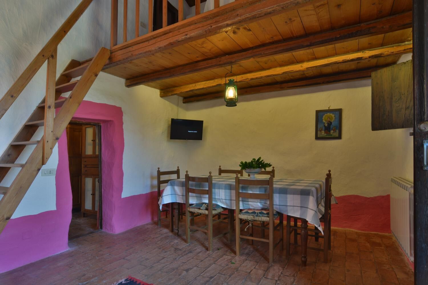 Un espace repas comprenant une table et des chaises en bois, un téléviseur fixé au mur et un escalier.