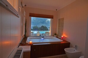 Un baño con una bañera grande, un bidé y ventana con vista a una piscina.