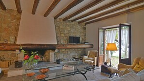 Una sala de estar rústica con chimenea de piedra, vigas de madera, una mesa de centro de vidrio y asientos cómodos.
