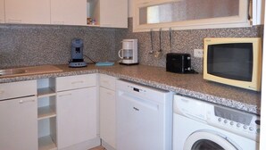 A compact kitchen with white cabinets, a coffee maker, a microwave, and a dishwasher.