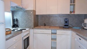 A compact kitchen with white cabinets, a granite countertop, a stove, an oven, a coffee maker, and a sink.