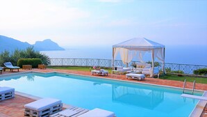 Un espace piscine avec des chaises longues, un auvent et une vue sur la mer.