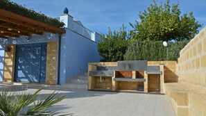 A patio area with a stone barbecue, a pergola, and a large door. - Villa Pigna Blue (Noto)