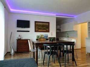 Un soggiorno moderno con angolo pranzo, cucina e TV a parete.
