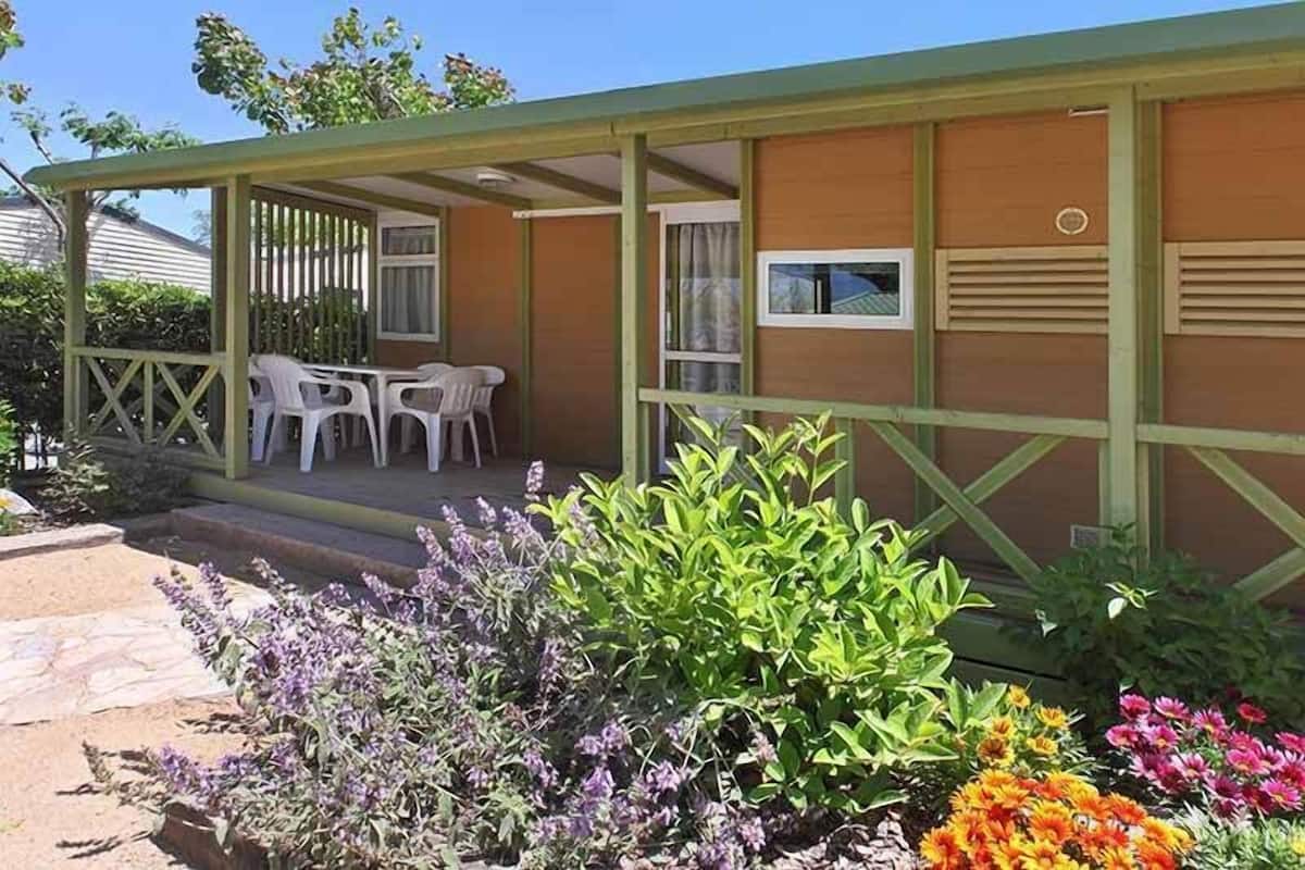 Uma área externa coberta com mesa e cadeiras, rodeada por diversas plantas e flores.