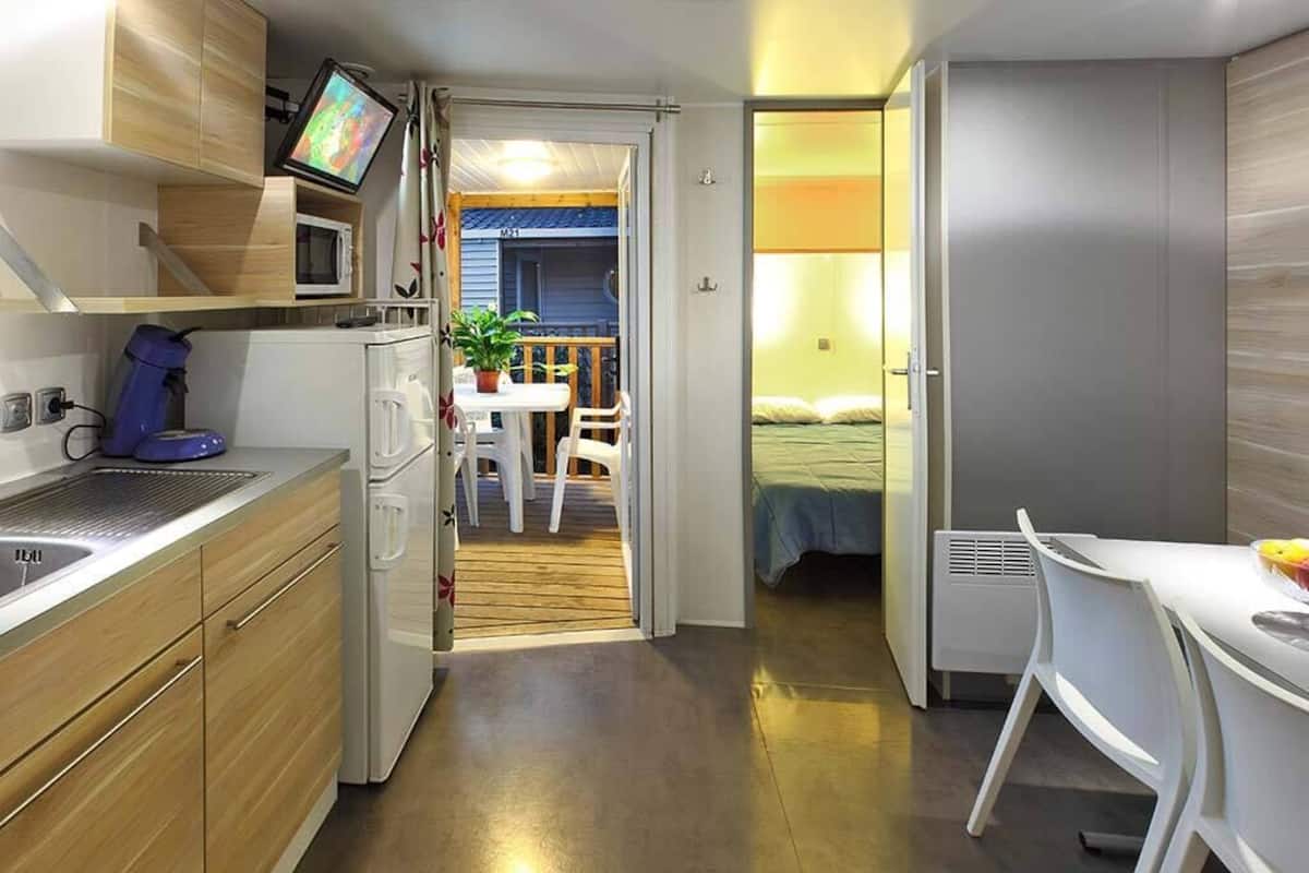 Quarto compacto com cozinha compacta, cama e pequena área de refeições.