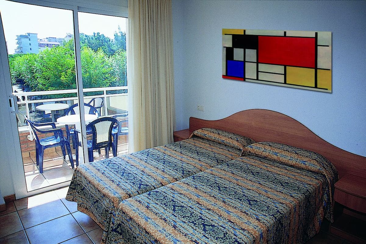 Quarto com uma cama, vista para o verde lá fora e uma mesa com cadeiras.