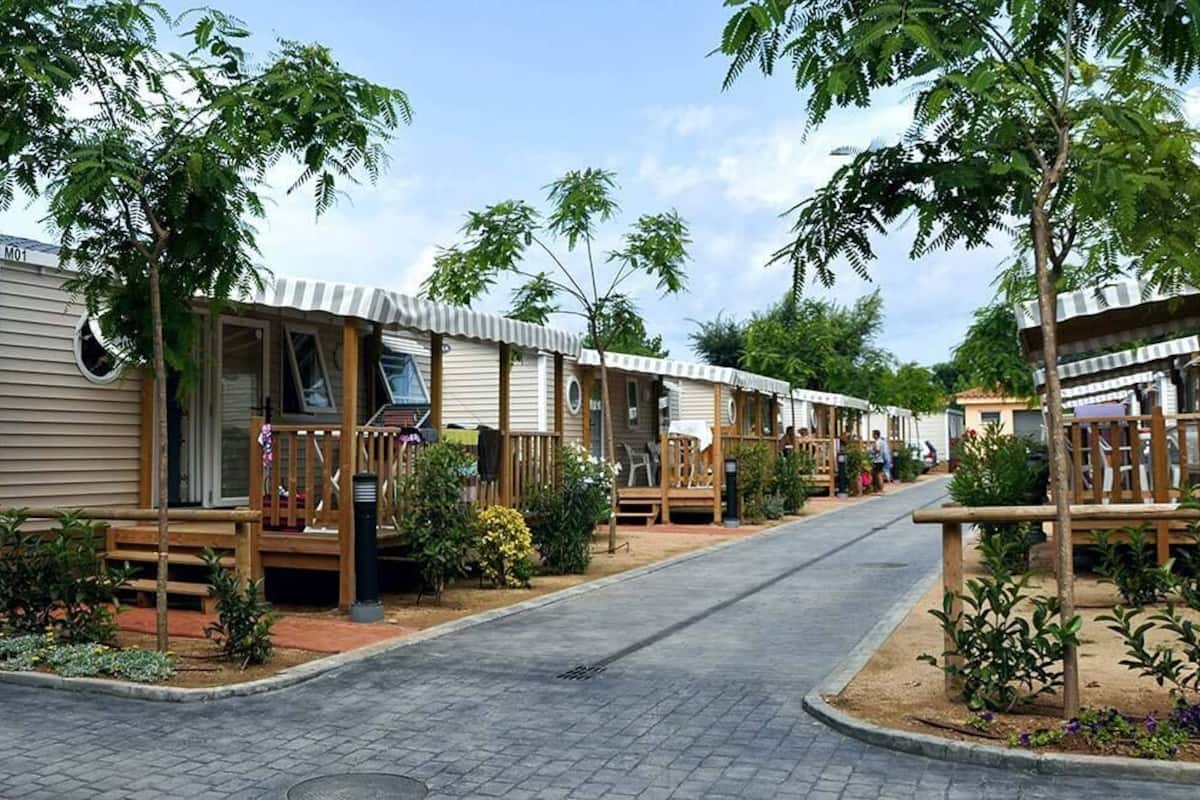 Uma fileira de casas móveis com decks de madeira e pequenos jardins, interligadas por um caminho pavimentado.
