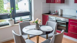 A modern kitchen with a round dining table, grey chairs, and red cabinets. - Business Apartments Ost (Ratingen)