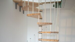 A spiral staircase with wooden steps and white railings in a room with wooden flooring and a gray sofa. - Business Apartments Ost (Ratingen)