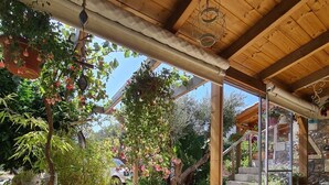 A covered patio area with a wooden ceiling, a cushioned bench, potted plants, and a stone staircase leading to an upper level. - Studio for Couples -Traditional Stone built - Rural location (Kefalas nr Vamos) (Kefalas)