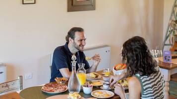 Una mesa de comedor con diversos alimentos para el desayuno, incluyendo platos de comida, una botella de jugo de naranja y una jarrón.