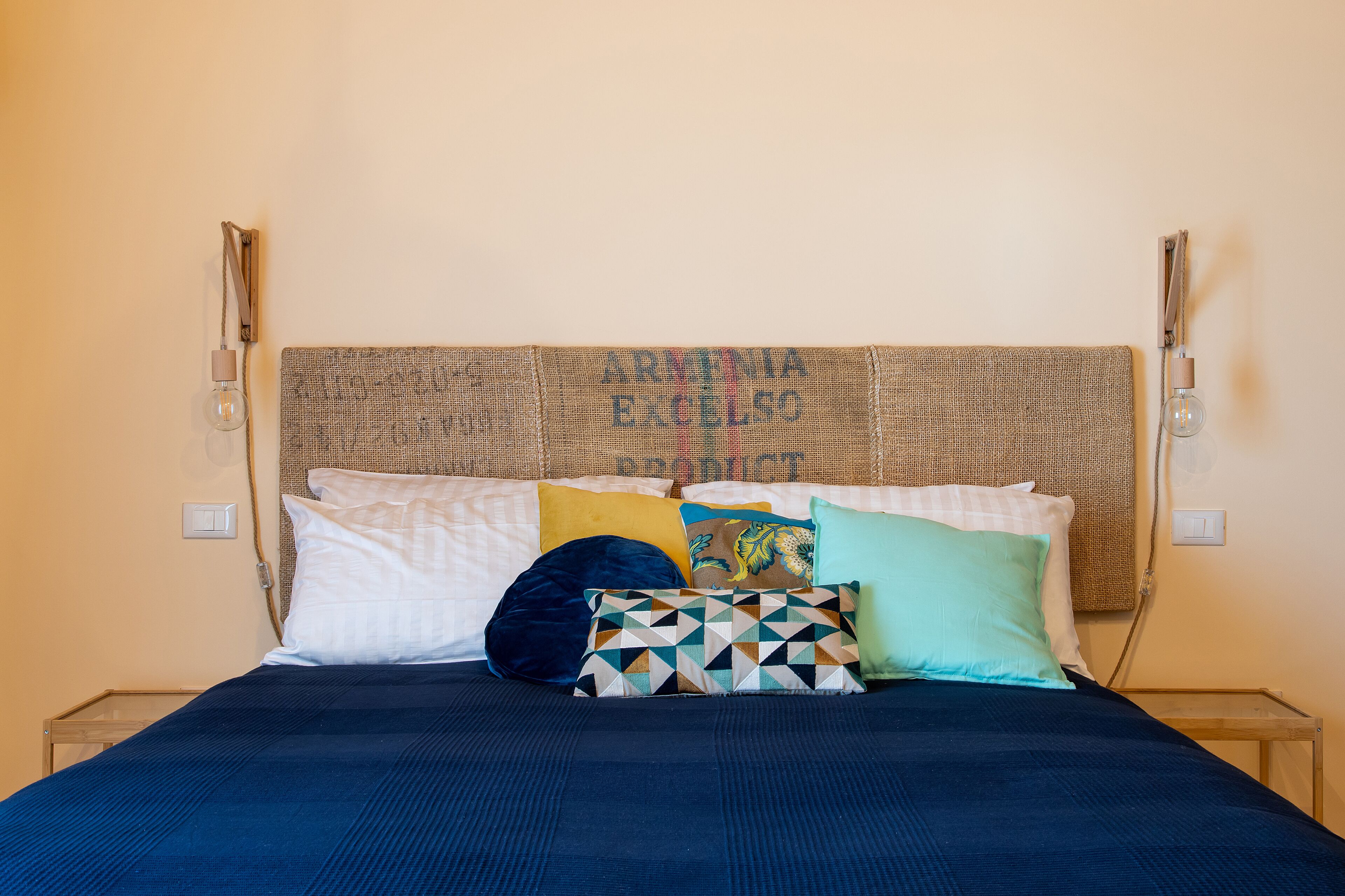 Een bed met een donkerblauwe spreideken en meerdere kussens, waaronder een kussen met een geometrisch patroon en een effen wit kussen.