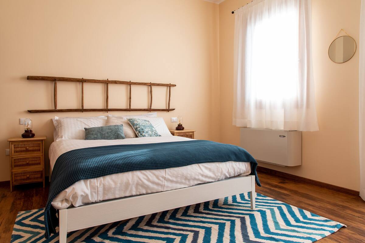 A neatly made bed with a blue and white checkered blanket, a wooden headboard, and a bedside table with a lamp.