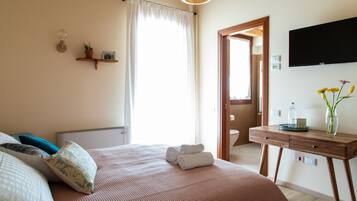 Une chambre à coucher comprenant un lit, des oreillers, une table de chevet avec un vase, un téléviseur à écran plat et une porte donnant accès à une salle de bain.