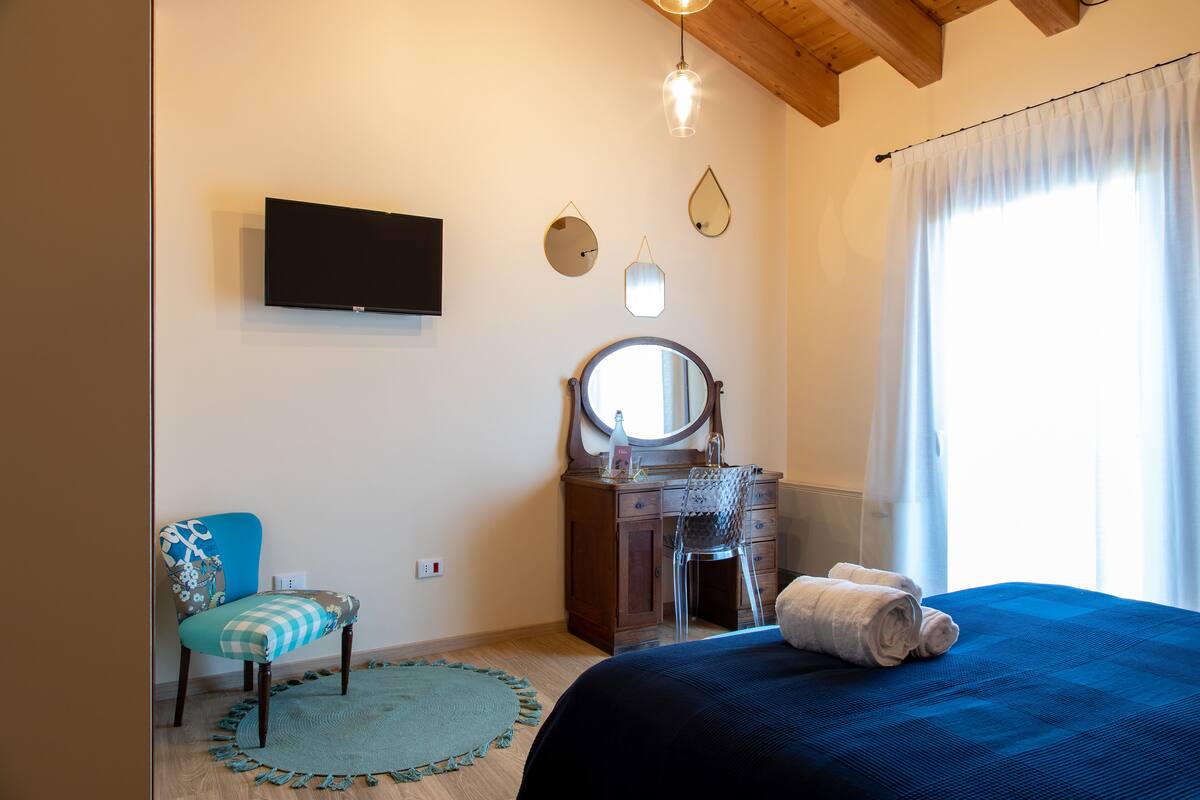A bedroom with a bed, a dresser, a chair, a mirror, and a TV on the wall.