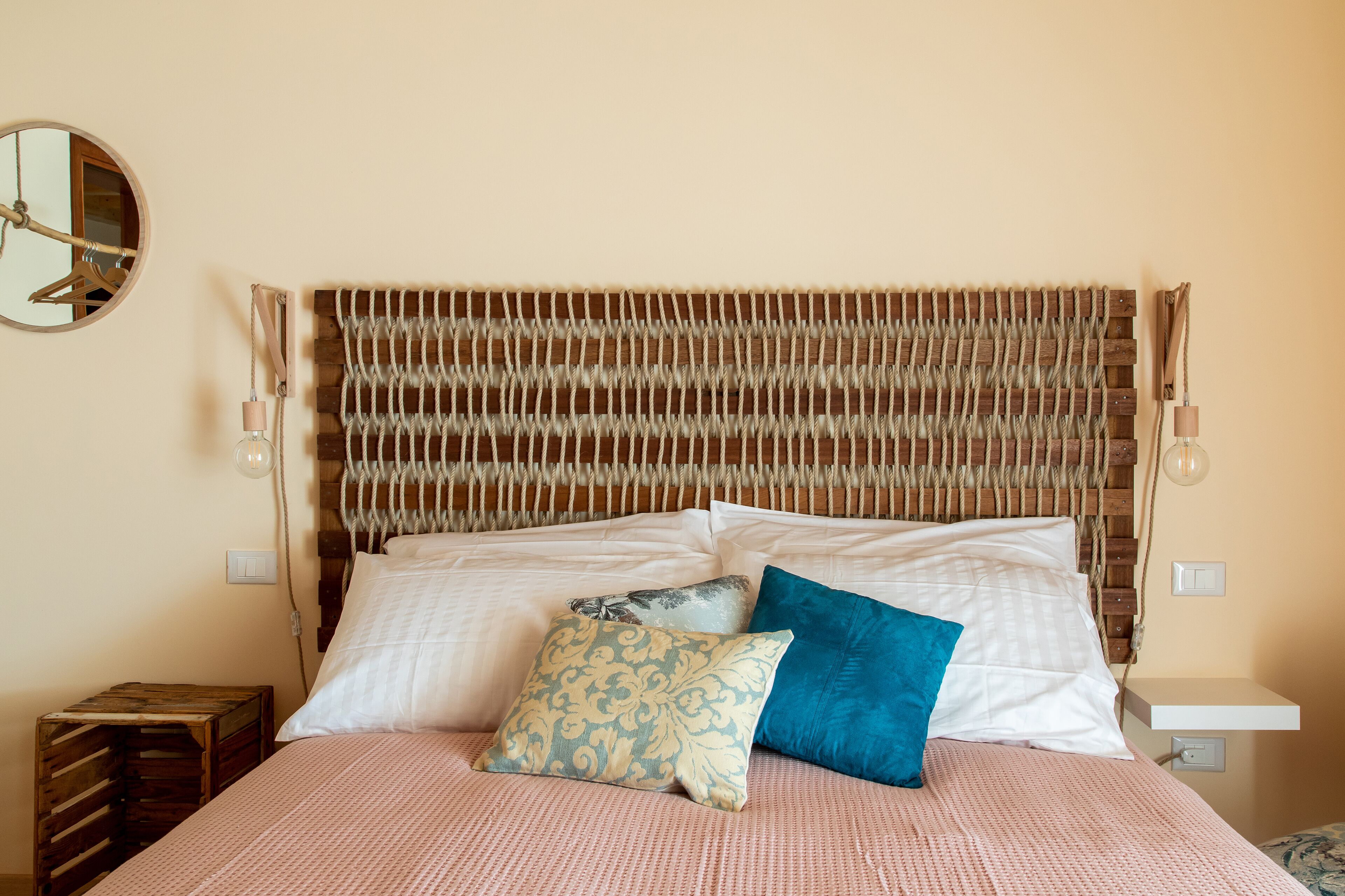 A bed with a woven headboard, two pillows, a bedside table, and a mirror on the wall.