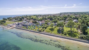 An aerial view of a coastal town with a beach, houses, and a large number of colorful beach huts. - Beach Side (Bembridge)