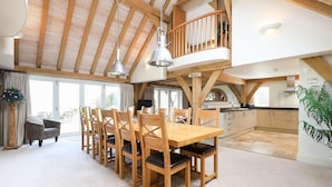 A spacious dining area with a high wooden ceiling, a balcony, and a kitchen in the background. - Beach Side (Bembridge)