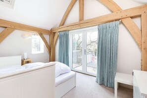 A bedroom with a bed, a bedside table, a window with curtains, and a view of the outside. - Beach Side (Bembridge)