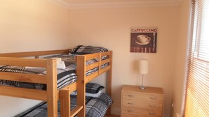 Una cama litera con ropa de cama a cuadros, una mesita de noche con una lámpara y un cartel en la pared.