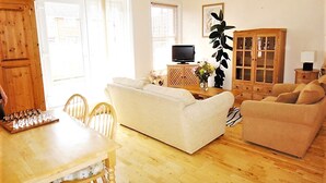 Una sala de estar con piso de madera, un sofá blanco, un sofá color beige, un mueble de madera y un televisor.