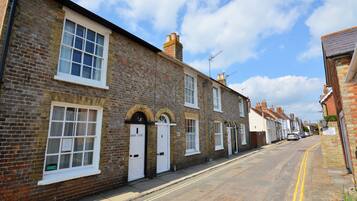 A row of traditional brick houses with white-framed windows and doors, a clear sky, and a double yellow line on the road.