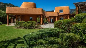 Un edificio con uno stile architettonico distintivo, caratterizzato da strutture arrotondate di colore arancione e un giardino curato con siepi verdi e fiori rossi.