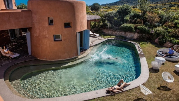 Una piscina con acqua cristallina, circondata da un solarium curvo, e una persona che si rilassa a bordo vasca.