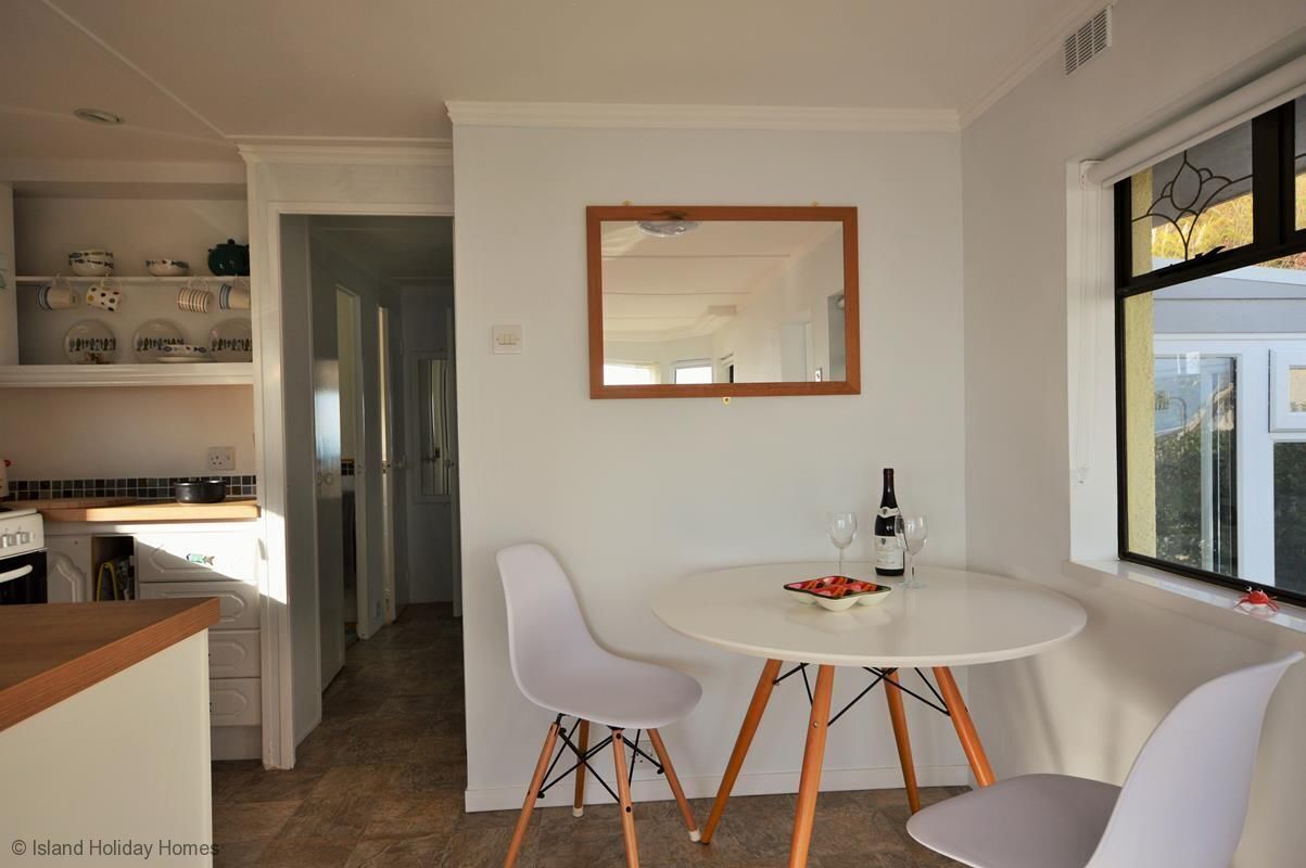 A modern kitchen with white cabinets, a dining area with a round table and two chairs, and a large window with a view.
