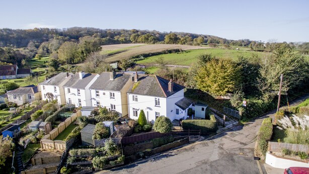 A residential area with a row of white houses, a driveway, and a green field in the background. - Charnwood Cottage (Sandown)