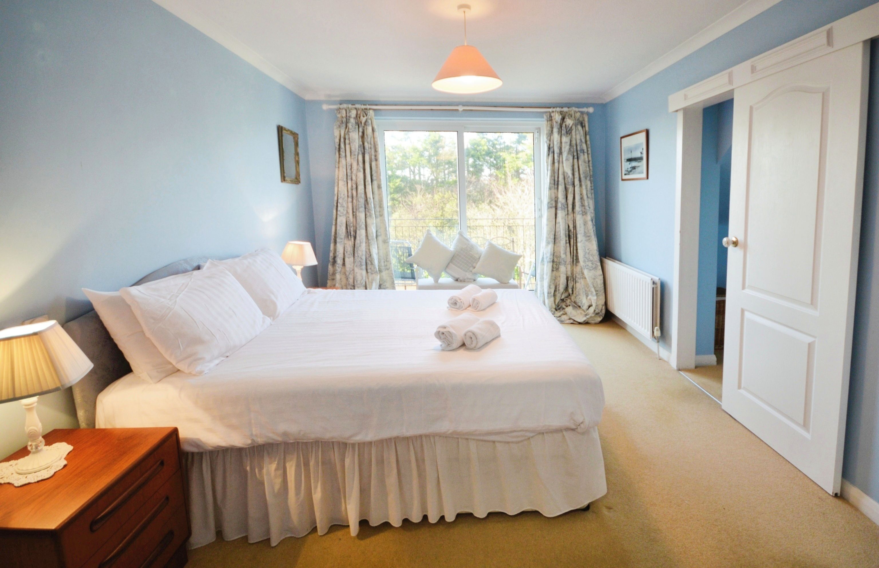A bedroom with a large bed, a nightstand, a window with curtains, and a door.